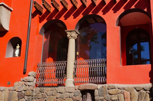 A red building with stone walls, arched windows, and a wrought iron balcony.