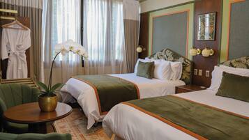 A hotel room with two beds, a sitting area with a table, and a potted plant.