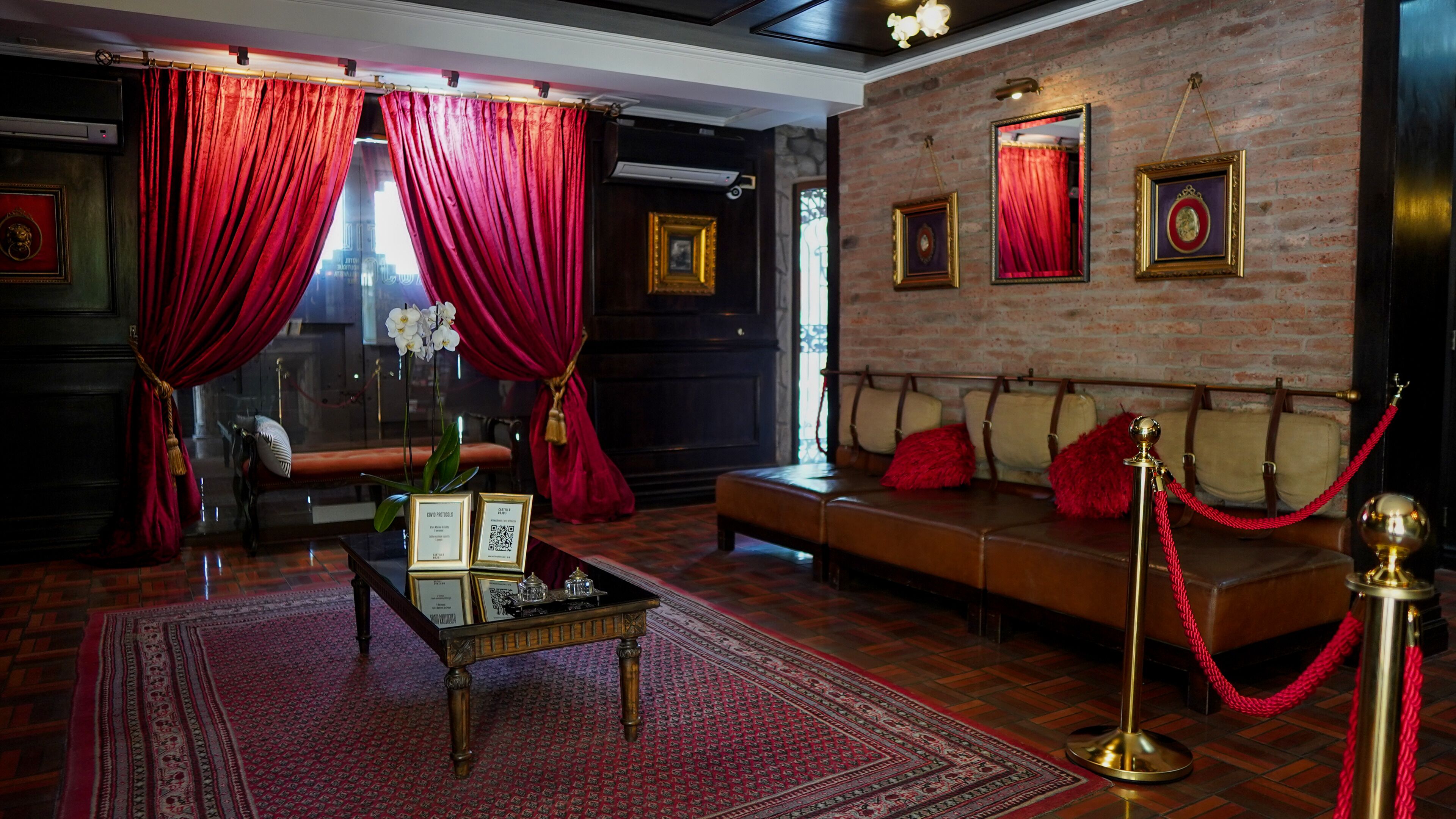 Una habitación con alfombra roja, un sofá con cojines rojos, una mesa con un florero y una barrera de cuerda roja.