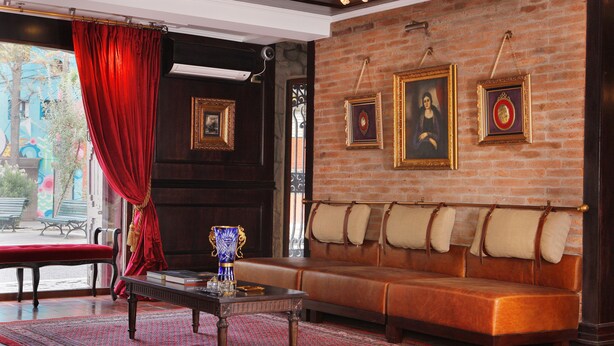 Une pièce avec un rideau rouge, un canapé, une table et des tableaux encadrés accrochés au mur.