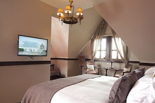 Una camera d'albergo con un letto grande, una televisione fissata al muro, un lampadario e una finestra con tende.