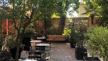 A patio area with tables and chairs, surrounded by potted plants and trees.