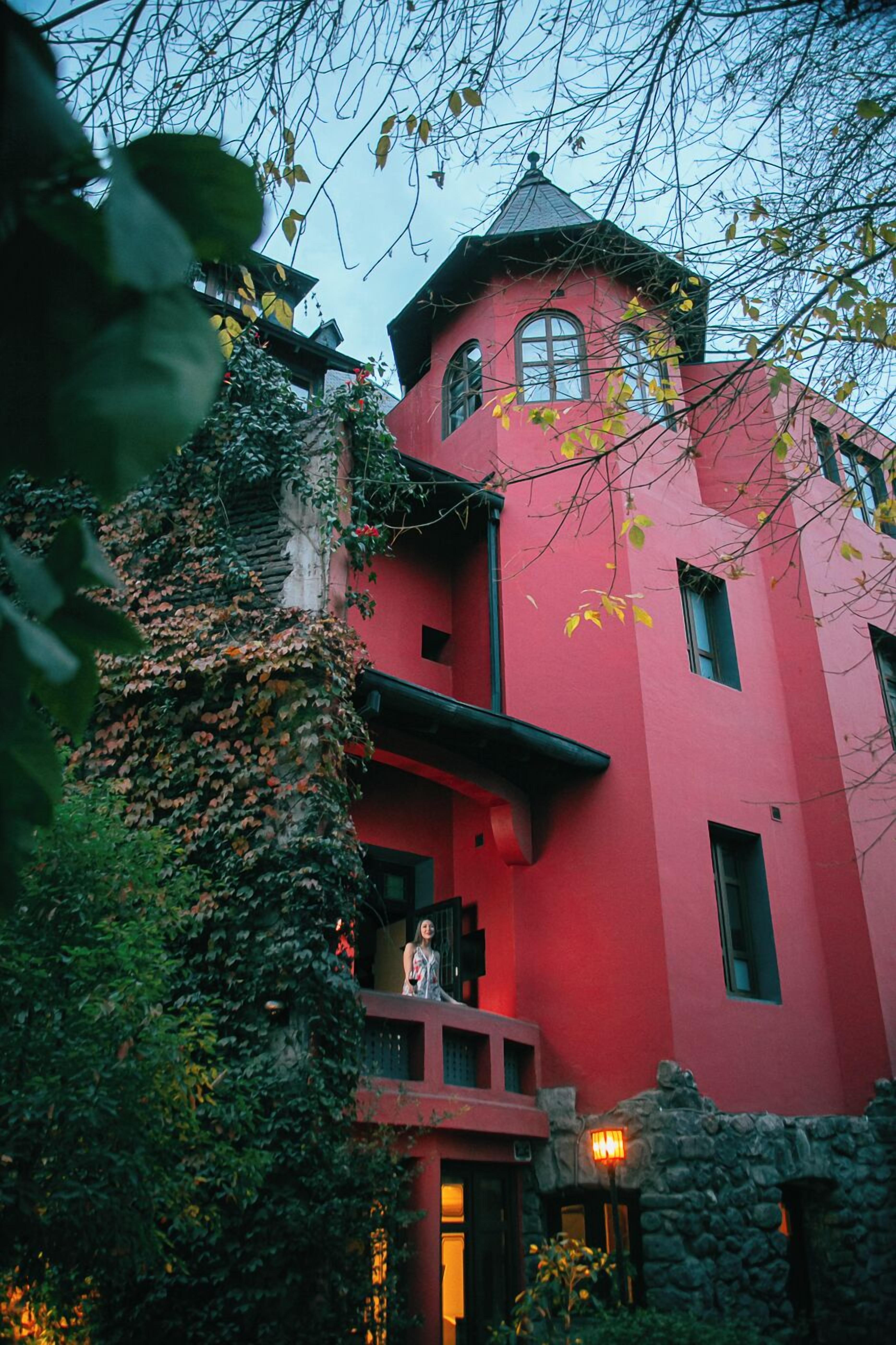 A red building with a tower, surrounded by greenery and ivy.