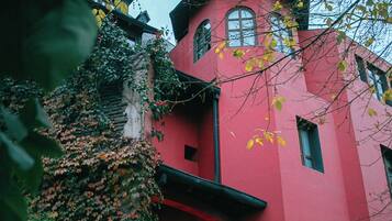 A red building with a tower, surrounded by greenery and ivy.