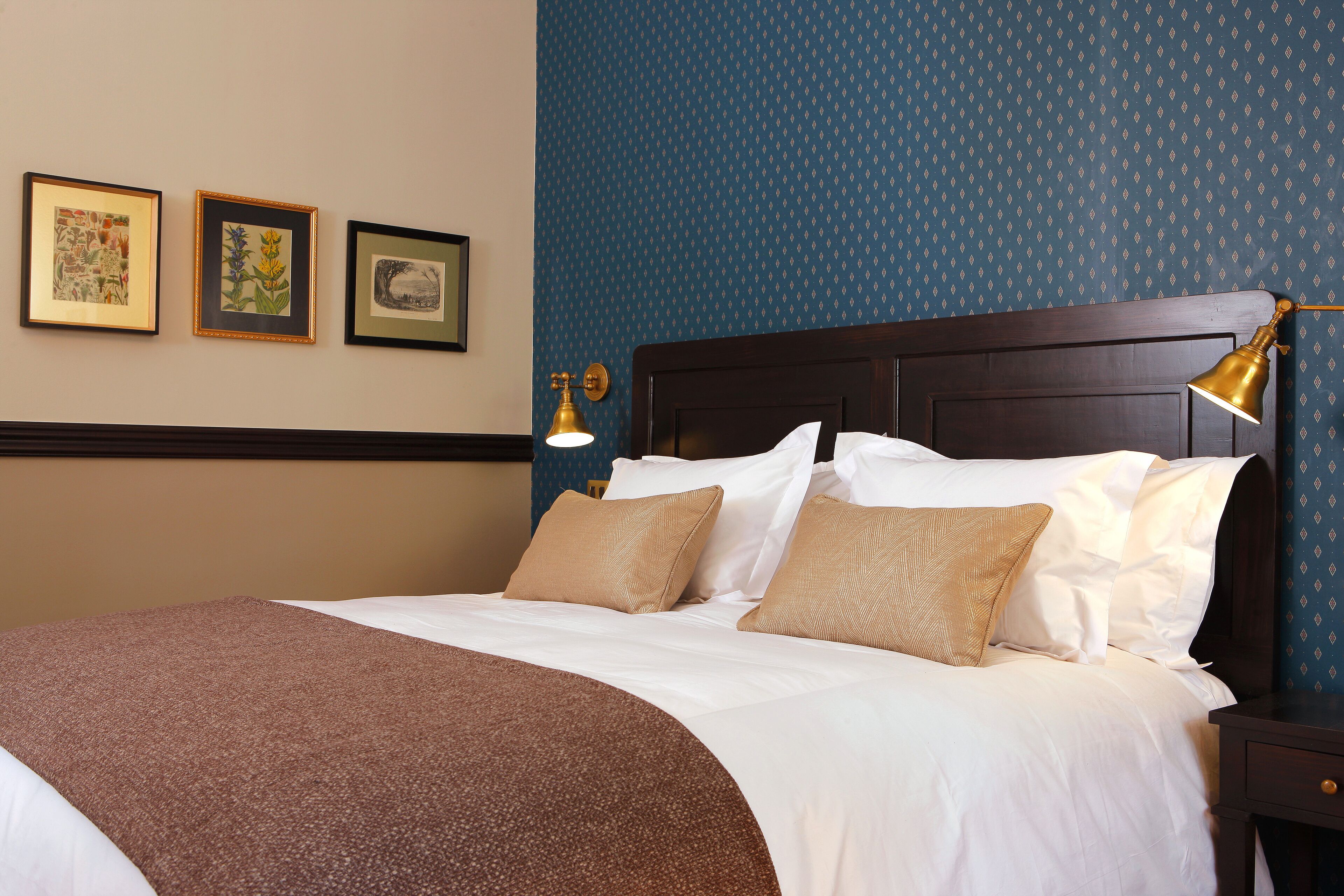 A neatly made bed with a brown throw blanket, white linens, and two beige pillows. There are three framed pictures on the wall above the bed.