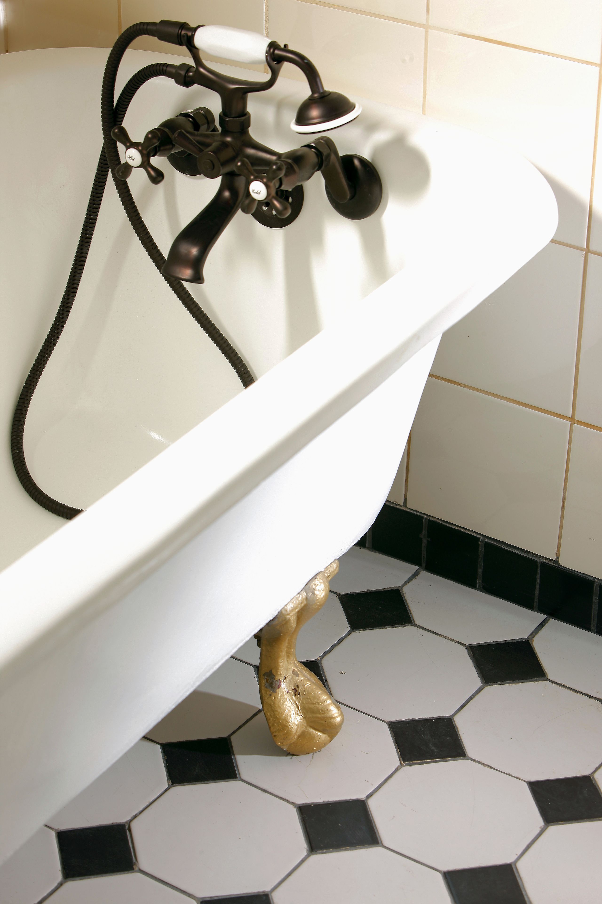 A white bathtub with a black faucet and hose, set against a tiled floor with a black and white pattern.