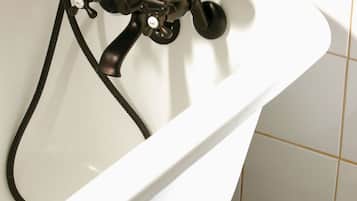 A white bathtub with a black faucet and hose, set against a tiled floor with a black and white pattern.