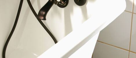 A white bathtub with a black faucet and hose, set against a tiled floor with a black and white pattern.