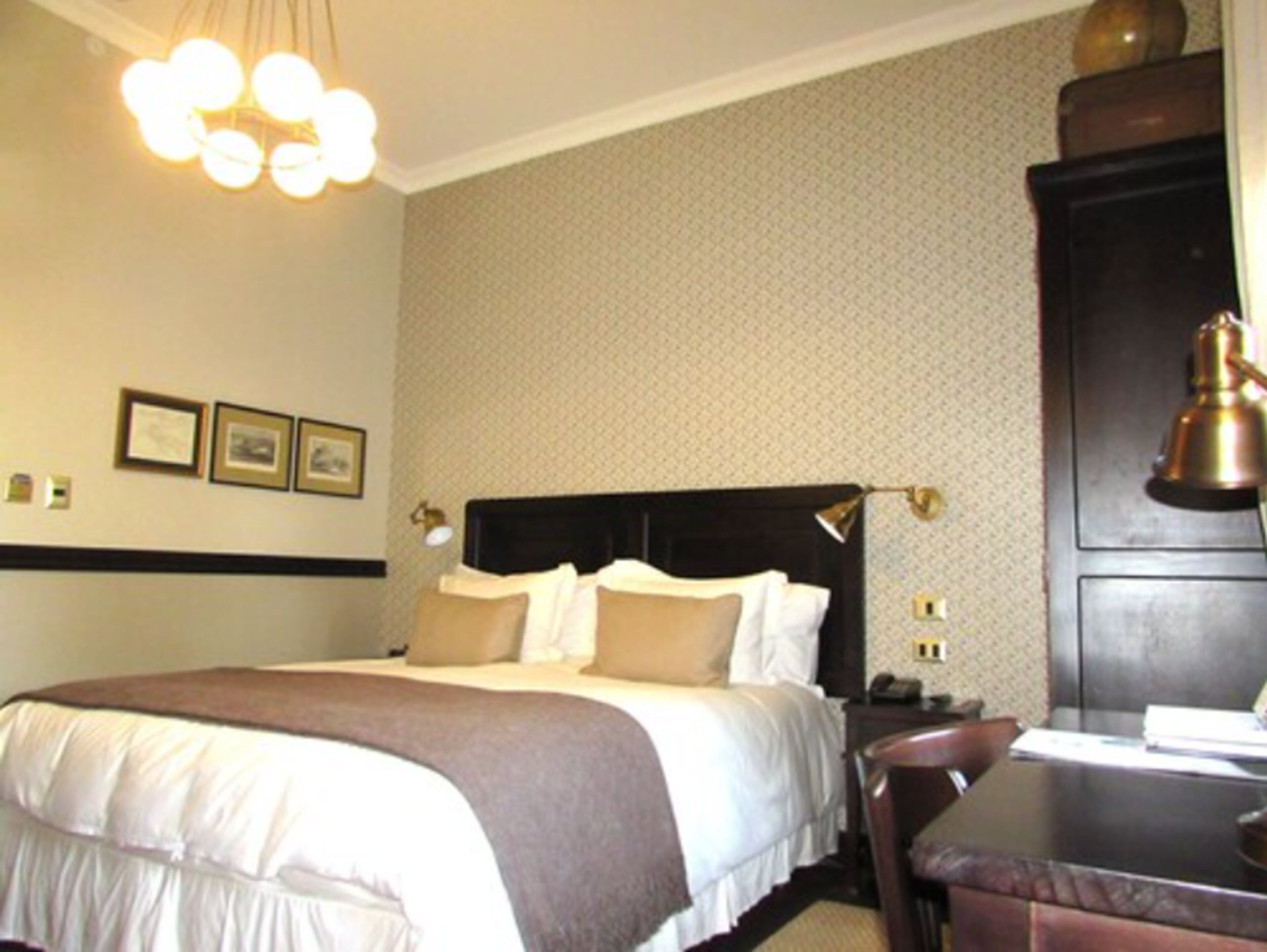 A hotel room with a bed, bedside table, lamp, and wall-mounted pictures.