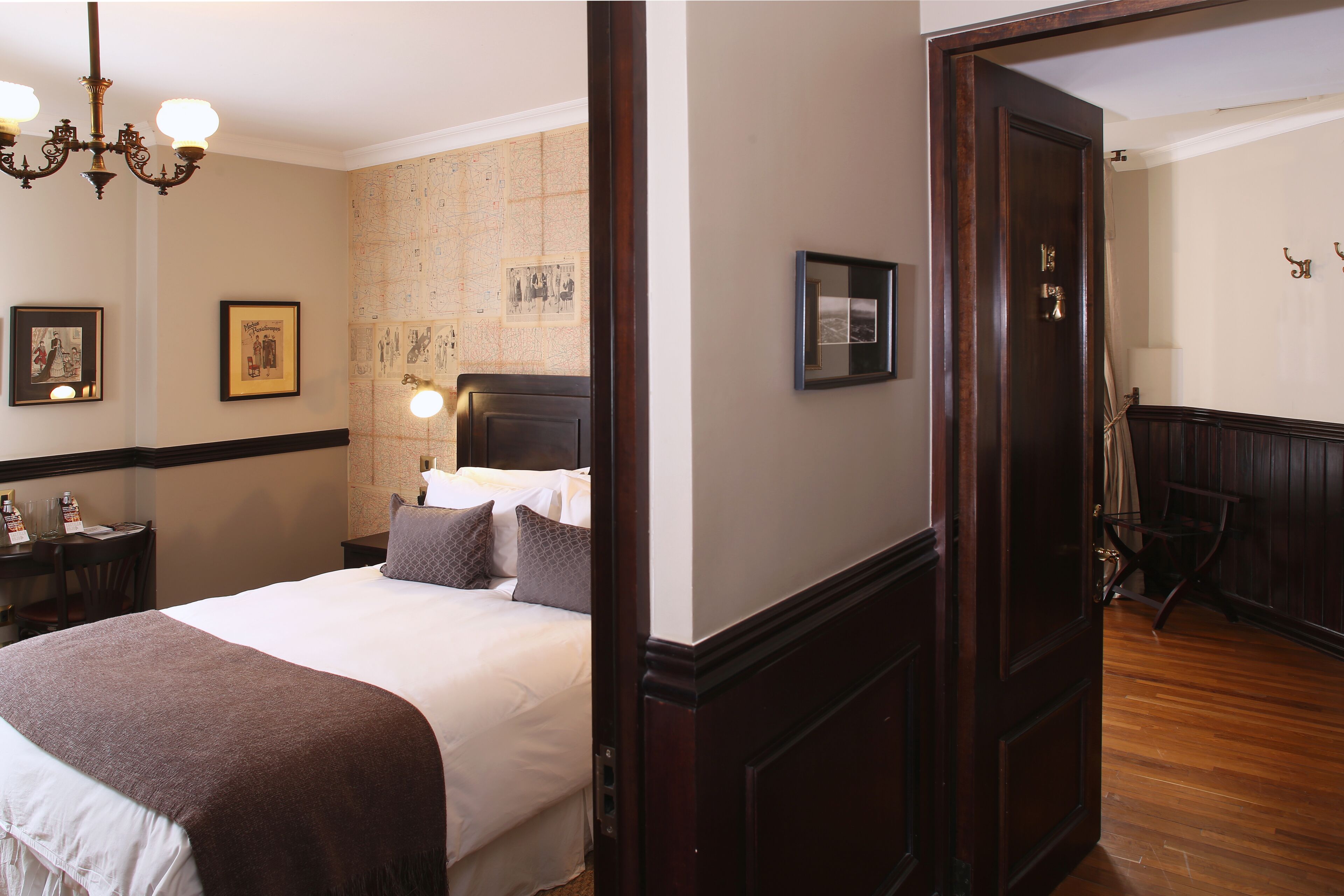 A hotel room with a large bed, a wooden dresser, a desk with a chair, and a chandelier.