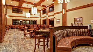A spacious dining area with wooden flooring, multiple tables and chairs, a curved leather bench, and pendant lighting.