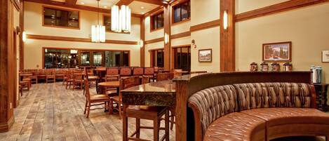 A spacious dining area with wooden flooring, multiple tables and chairs, a curved leather bench, and pendant lighting.