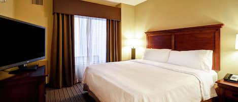 A hotel room with a large bed, a flat-screen TV, a ceiling fan, and a bedside table with a lamp.