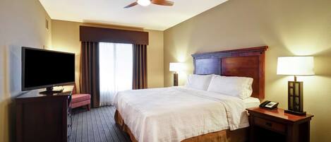 Una habitación de hotel con cama, televisión, escritorio, lámpara y ventilador de techo.