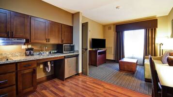 Una habitación de hotel con cocina, zona de estar con sofá y mesa, y televisor.