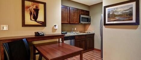 A dining area with a wooden table and chairs, a microwave, and a refrigerator in the kitchen area.