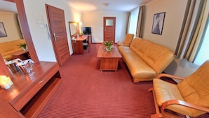 Et hotelværelse med rødt tæppe, et træskrivebord med lampe, en sofa og en lænestol.