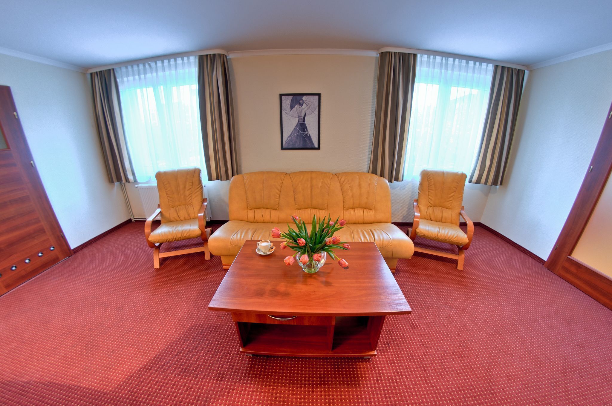 A room with a sofa, two armchairs, a coffee table, and a painting on the wall.