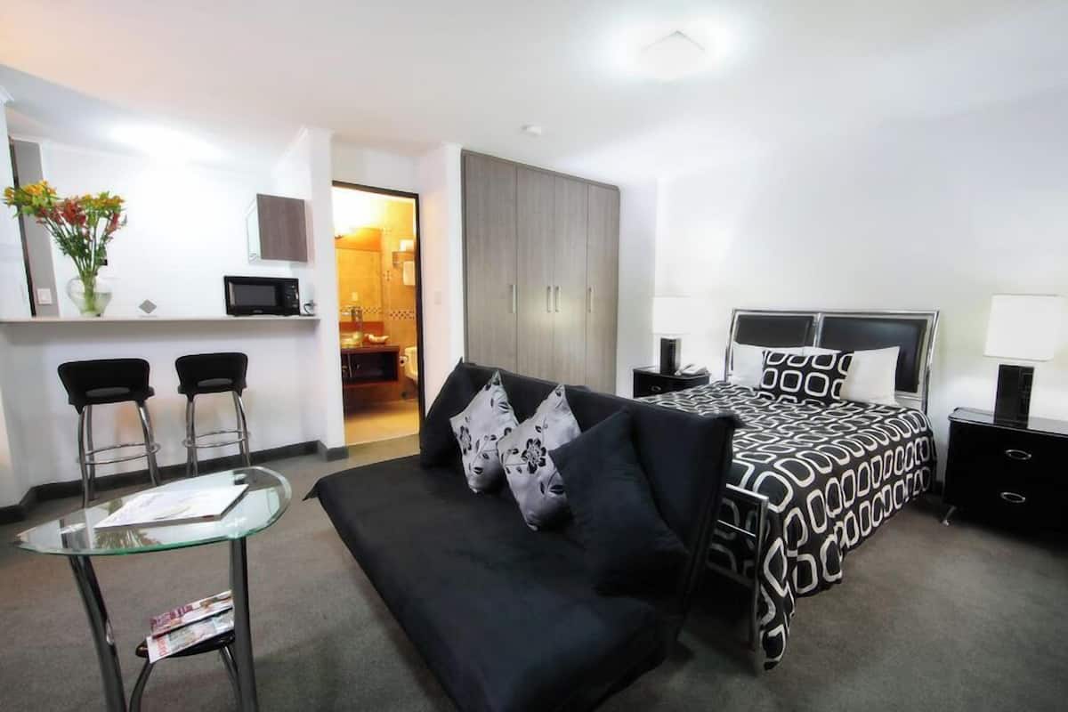 A modern hotel room with a black and white patterned bed, a black sofa, a glass coffee table, and a TV on a stand.