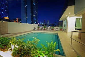 Piscina en la azotea con vista a la ciudad, sillas de descanso y plantas en macetas.