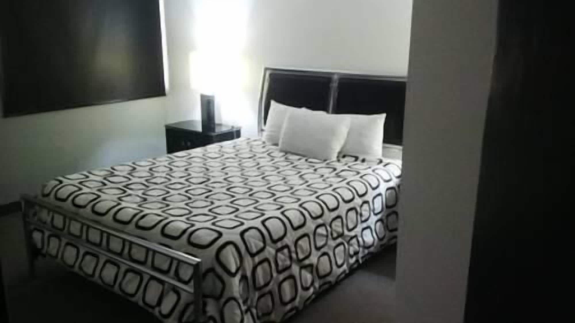 A bedroom with a patterned bedspread, a nightstand, and a window with blinds.