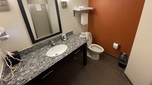 Un baño con encimera de granito, lavamanos, inodoro, espejo y toallero.