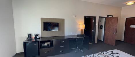Una habitación de hotel con cama, escritorio, televisor de pantalla plana, lámpara y armario.