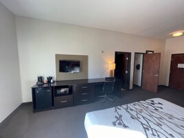 A hotel room with a bed, a desk with a flat-screen TV, a lamp, and a wardrobe.