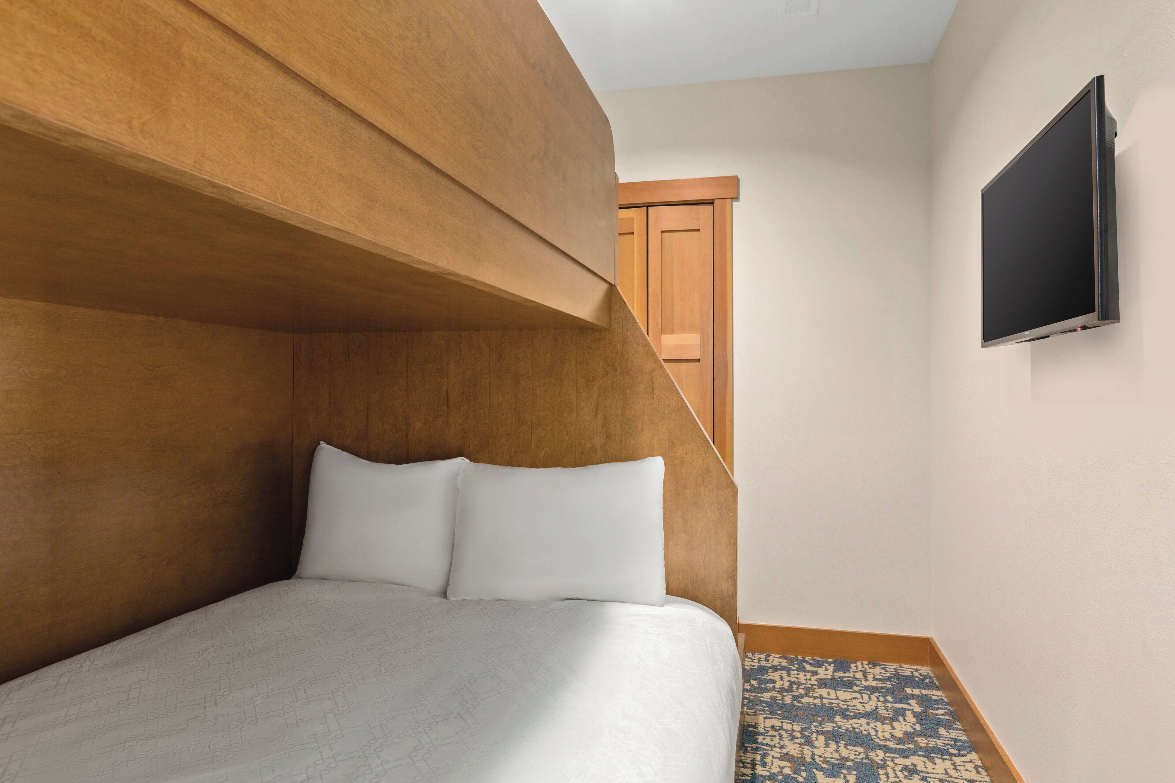 A bedroom with a bed, wooden headboard, and a flat-screen TV on the wall.