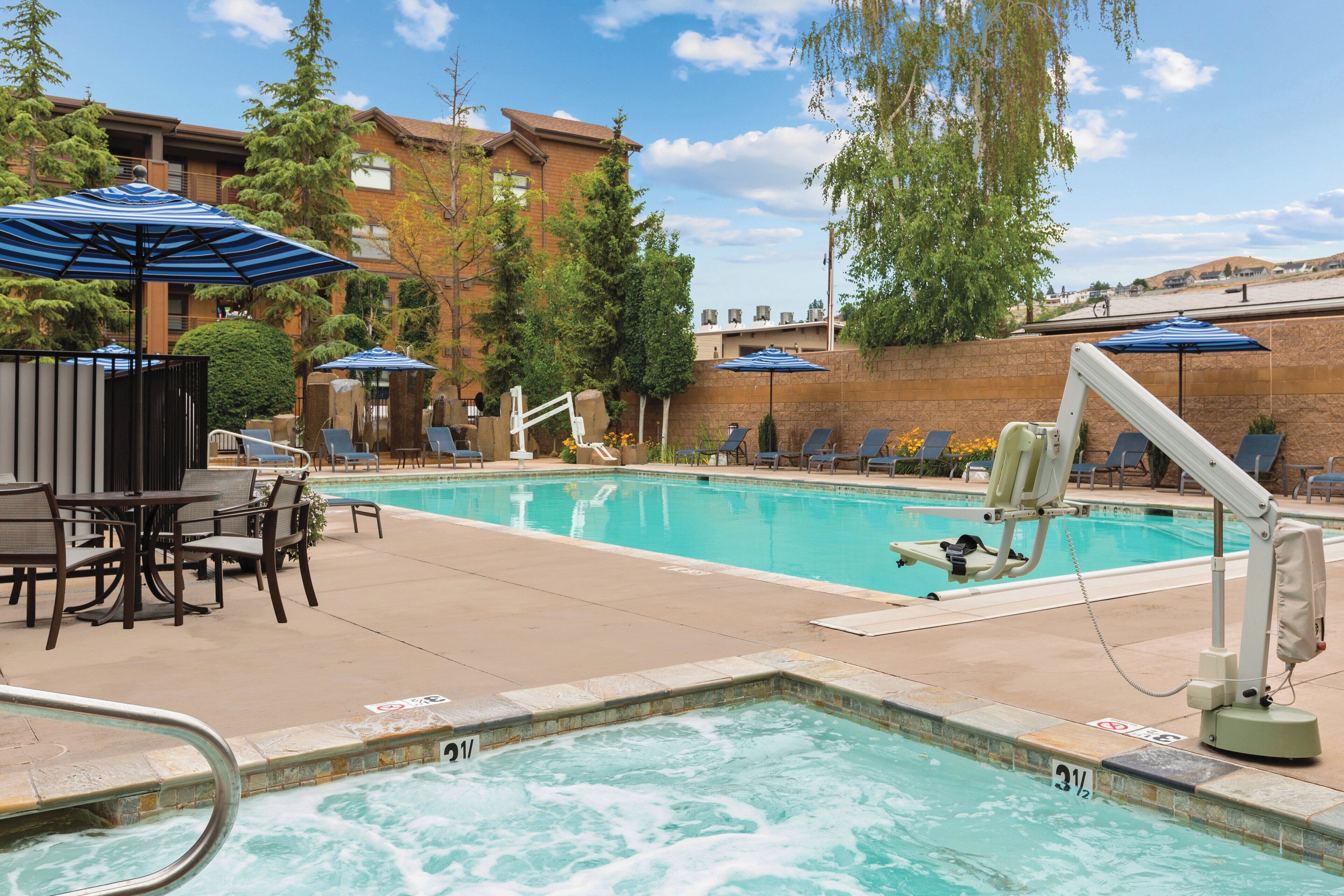 A swimming pool with lounge chairs and umbrellas, surrounded by brick buildings and trees.