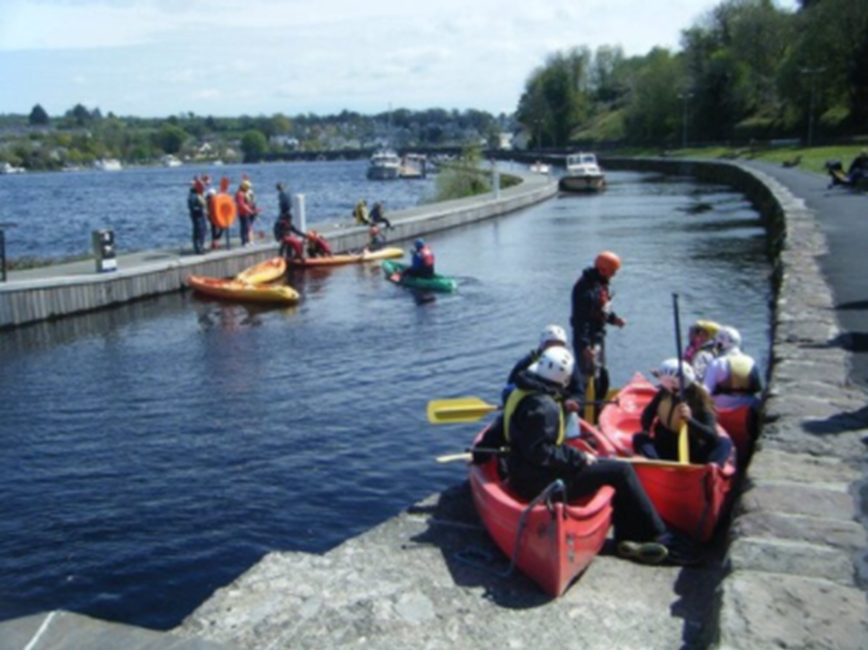 A group of people in kayaks and a red boat on a calm waterway.