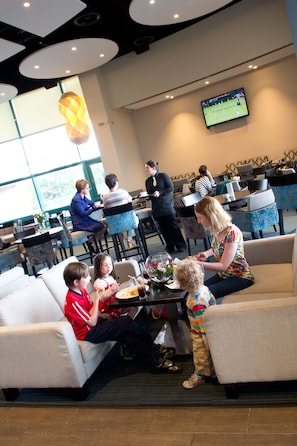 Une famille prend son repas dans un restaurant moderne doté d’un grand écran de télévision, de sièges confortables et d’une ambiance décontractée.