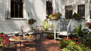 Une terrasse avec une table préparée pour le petit-déjeuner, des sièges d’extérieur et des plantes en pot.