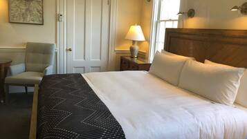 A neatly made bed with white linens, a chair, a lamp, and a map on the wall.