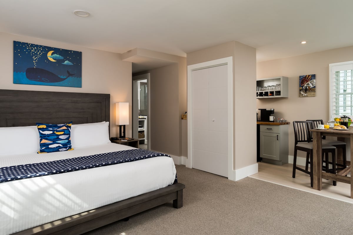 A hotel room with a large bed, a desk, and a kitchenette.