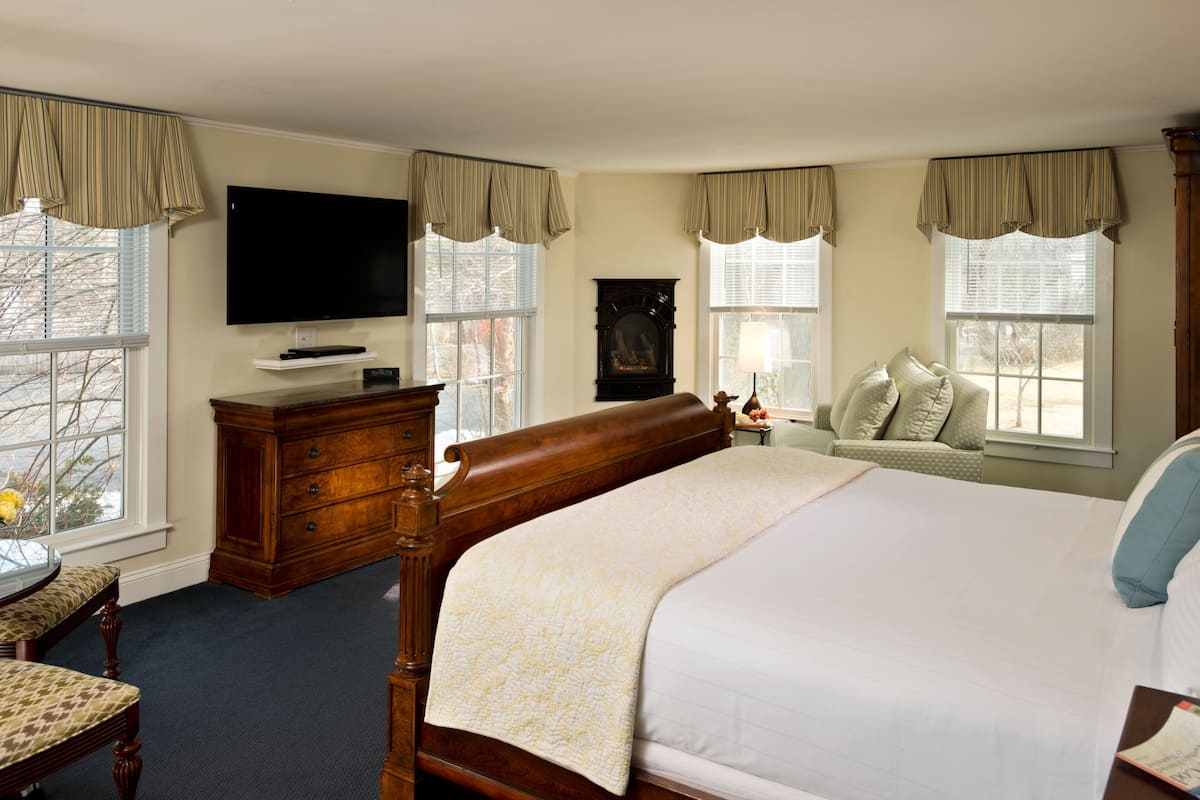 A bedroom with a large bed, a dresser, a television, and a fireplace.