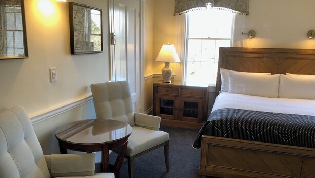 Habitación de hotel con cama, dos sillones, una mesita, lámpara y ventana con cortinas.