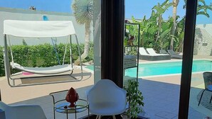 Een kamer met uitzicht op een zwembad, een stoel, een tafel en een kleine plant.