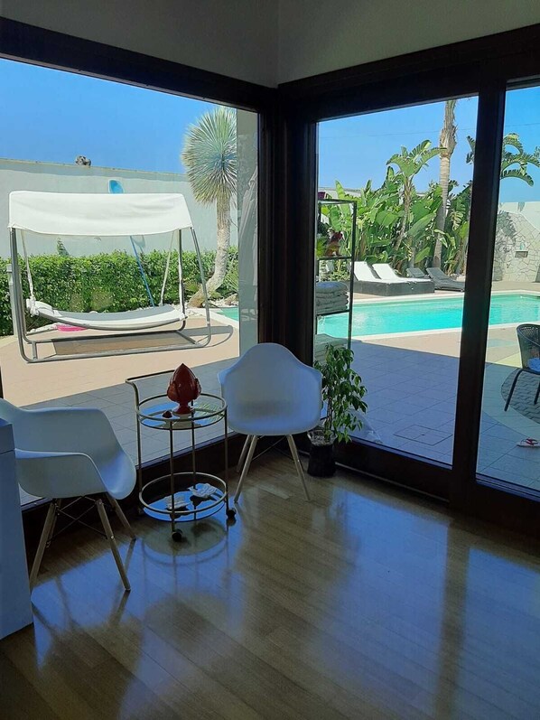 Habitación con vista a una piscina, una silla, una mesa y una planta pequeña.