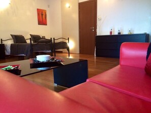 Ein modernes Wohnzimmer mit einem roten Sofa, einem schwarzen Couchtisch und einem Bett mit grauer Bettwäsche.