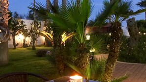 Een terras buiten met een glazen tafel, een brandende kaars en palmbomen.