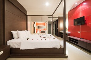 A modern hotel room with a large bed, a TV mounted on the wall, and a red accent wall.