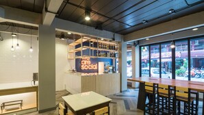 A modern bar area with a wooden counter, seating, and a view of the street through large windows. - Alfresco Phuket Hotel (Patong)
