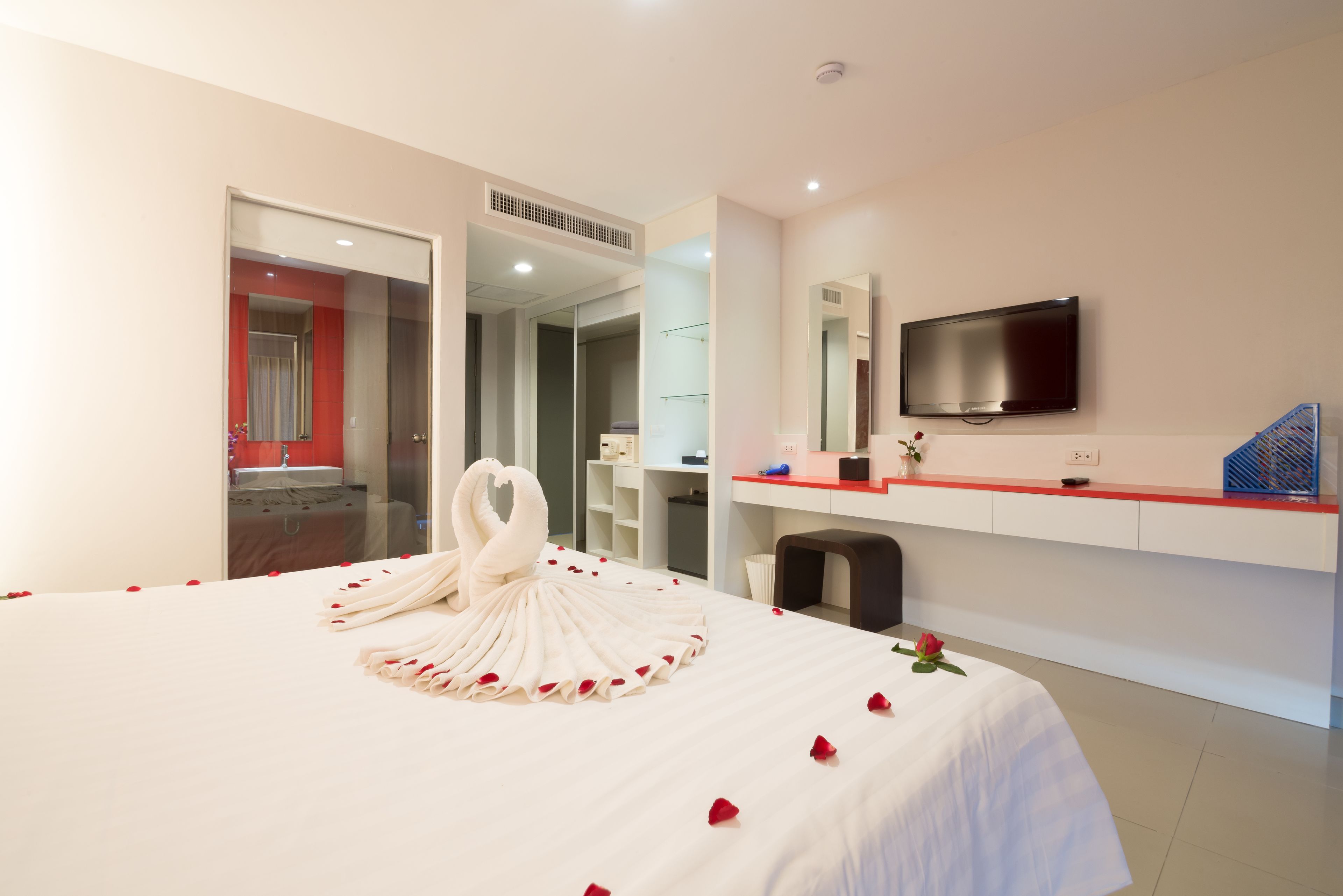 A hotel room with a bed, a TV, a desk, and a bathroom visible through an open door.