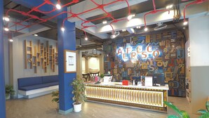 A reception area with a blue sofa, a reception desk, potted plants, and a wall with alphabet letters. - Alfresco Phuket Hotel (Patong)