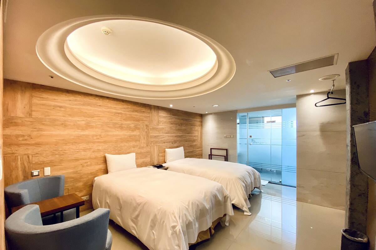 A modern hotel room with two beds, a seating area, and a large mirror.