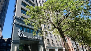 A modern building with a sign for the Burgundy Hotel. It features a large entrance with a gated driveway and a tree in the foreground. - Burgary Hotel (Taipei)
