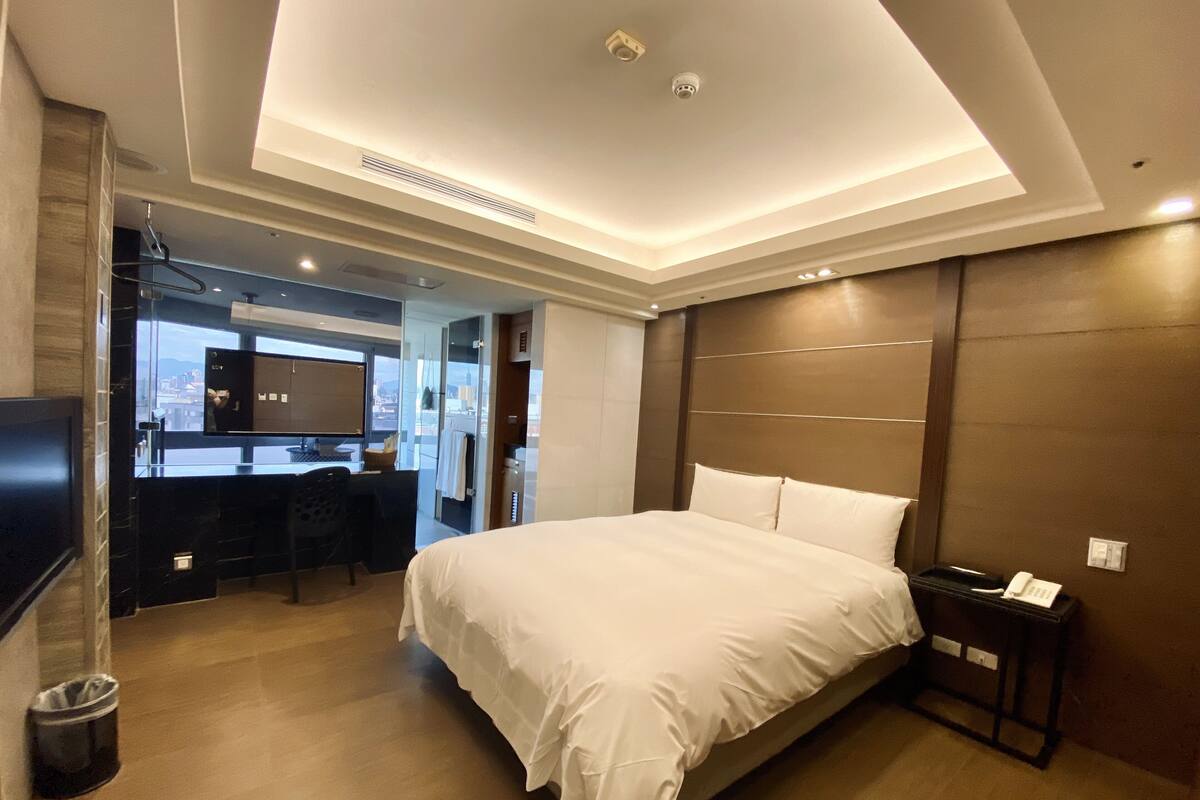 A modern hotel room with a large bed, a desk, and a view of the city.