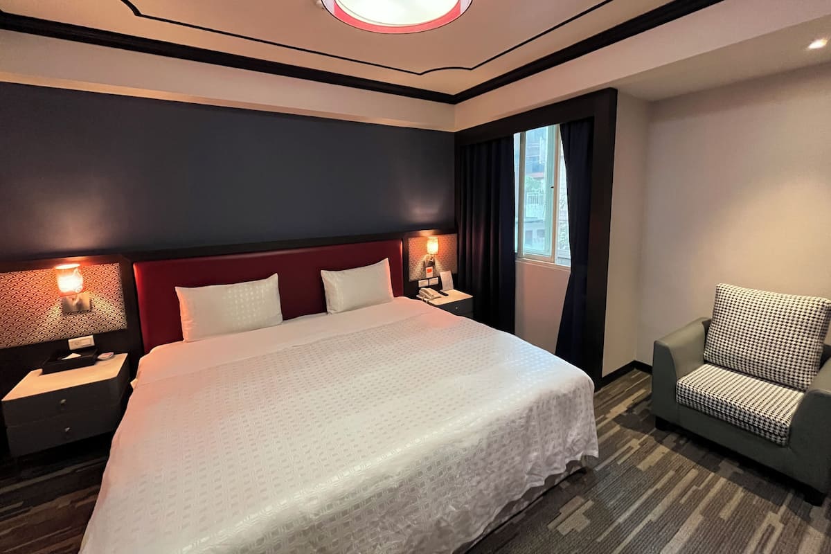 A hotel room with a large bed, two bedside tables with lamps, a chair, and a window with curtains.