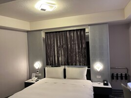 Habitación de hotel con cama, dos mesitas de noche, un teléfono, un control remoto, una lámpara y un espejo.